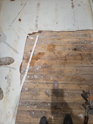 Rénovation de sol Sol en bois avec des zones abîmées et des traces de nettoyage.